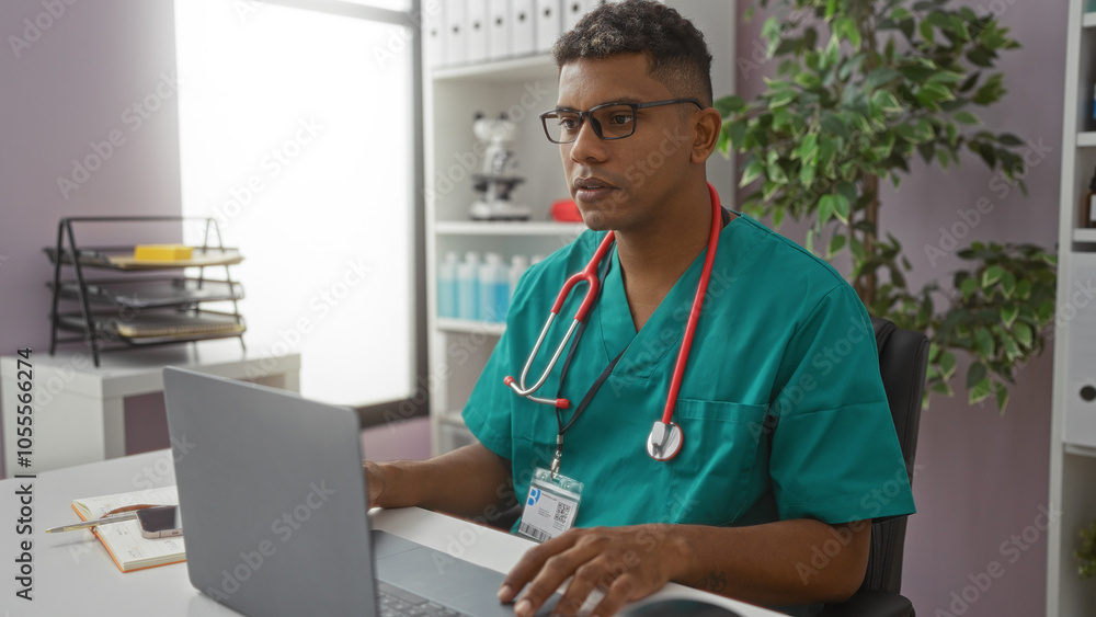 Young hispanic man working on a laptop in a clinic wearing medical scrubs, with a stethoscope around his neck and an identification badge in an interior workplace setting. Young hispanic man working on a laptop in a clinic wearing medical scrubs, with a stethoscope around his neck and an identification badge in an interior workplace setting.