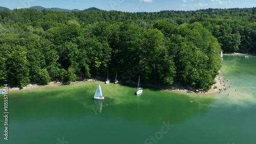 Flying over the lake with a view of the mountains and boats floating by the shore. Beautiful colors of summer. Mavic 3