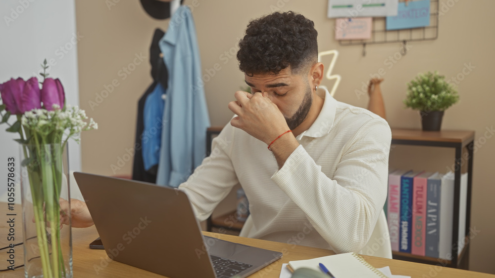 Stressed hispanic man using laptop in home office with flowers, bookshelf and casual wear. Stressed hispanic man using laptop in home office with flowers, bookshelf and casual wear.