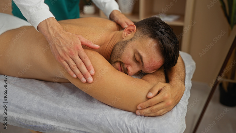 Man enjoying relaxing massage from masseur in wellness room with calm interior atmosphere Man enjoying relaxing massage from masseur in wellness room with calm interior atmosphere