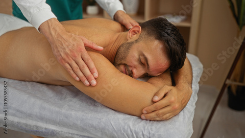 Man enjoying relaxing massage from masseur in wellness room with calm interior atmosphere