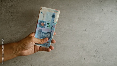 Wallpaper Mural Man's hand holding chinese yuan notes against a concrete background, highlighting the details of currency and human touch. Torontodigital.ca