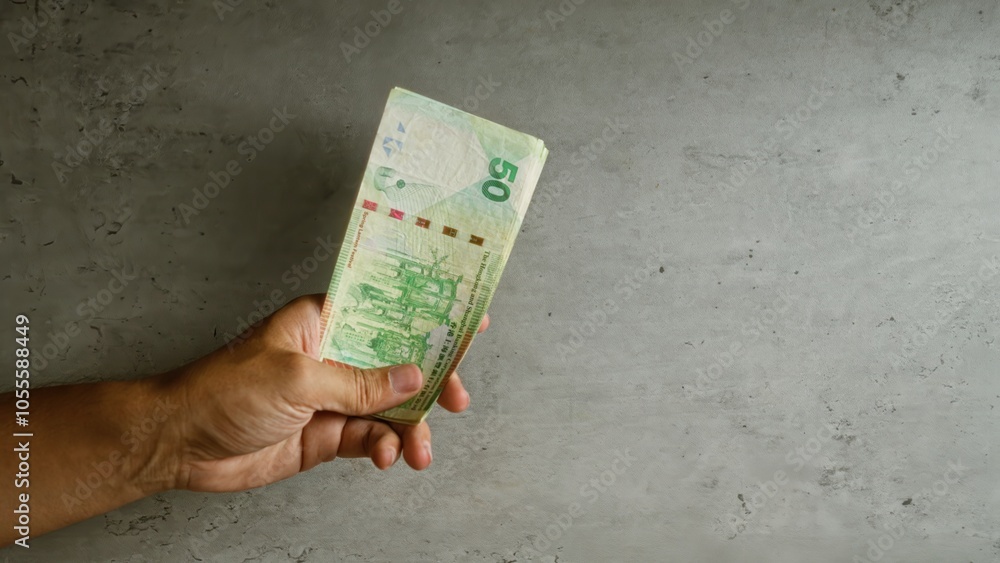 Hand holding hong kong dollars against a concrete background, showcasing asian currency in a financial context Hand holding hong kong dollars against a concrete background, showcasing asian currency in a financial context