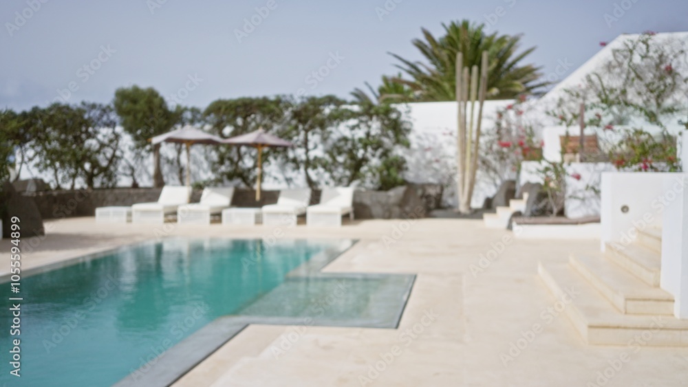 Fototapeta premium Blurred tropical resort with empty poolside chairs and lush greenery in the background, evoking a tranquil vacation ambiance