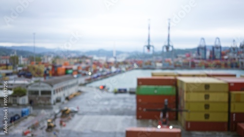 Blurred view of a busy port with shipping containers, cranes, and an overcast sky creating a defocused maritime industrial scene. photo