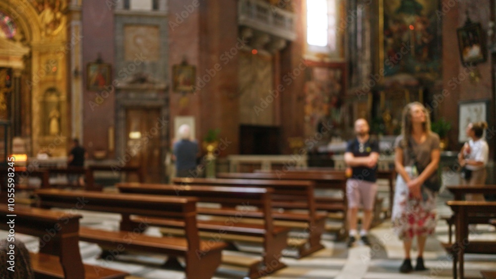 People standing indoors in a blurred, out of focus church setting with benches and religious artwork in the background, capturing a calm, contemplative atmosphere. People standing indoors in a blurred, out of focus church setting with benches and religious artwork in the background, capturing a calm, contemplative atmosphere.