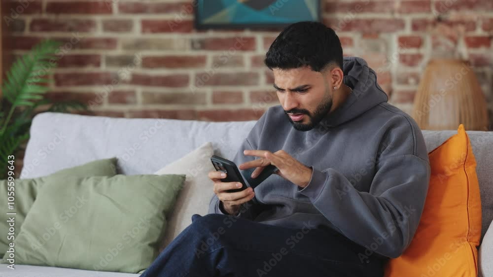 Young man in despair placing palm on face while getting annoyed with broken touchscreen of smartphone. Furious male not dealing with connection problems in apartment with bricky wall behind. Young man in despair placing palm on face while getting annoyed with broken touchscreen of smartphone. Furious male not dealing with connection problems in apartment with bricky wall behind.