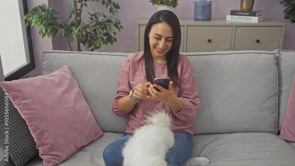 A smiling young woman using smartphone with her maltese dog on a couch in a cozy living room. A smiling young woman using smartphone with her maltese dog on a couch in a cozy living room.