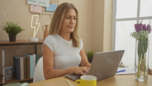 Mature blonde woman using laptop in a cozy interior home setting.