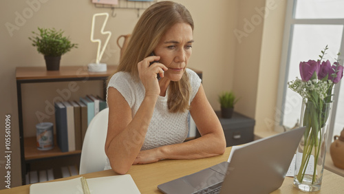 Mature woman using laptop and talking on phone in home office