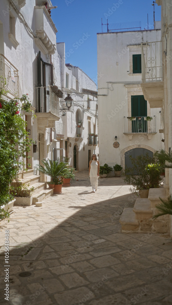 A beautiful young hispanic woman walks through the charming old town streets of locorotondo in puglia, italy, surrounded by white buildings and lush greenery. A beautiful young hispanic woman walks through the charming old town streets of locorotondo in puglia, italy, surrounded by white buildings and lush greenery.