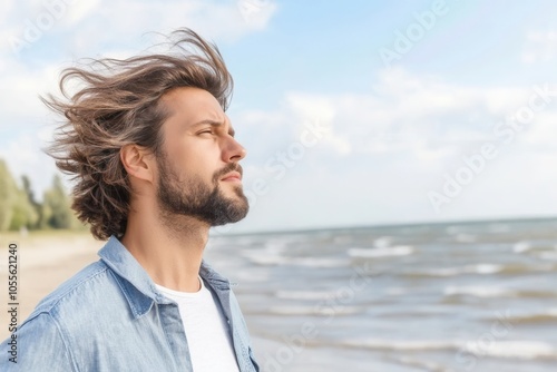 Standing by the ocean, a man embraces the soothing sea breeze as it gently tousles his hair. The dawn light casts a tranquil glow, enhancing the peaceful atmosphere of the beach, inviting calm reflect