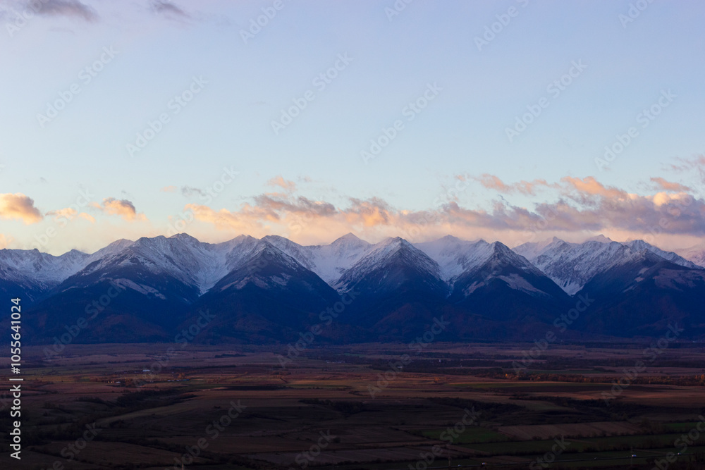 Carpathian mountain peaks view in the morning sunlight. Snow-covered slopes and cloudy sky. Transylvania is a region in central Romania. A popular ski resort is located nearby Carpathian mountain peaks view in the morning sunlight. Snow-covered slopes and cloudy sky. Transylvania is a region in central Romania. A popular ski resort is located nearby