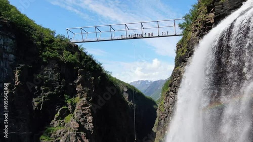 Aerial view of bungee jumper leaping from a bridge over a majestic waterfall in a scenic valley surrounded by cliffs and greenery, Birtavarre, Norway. photo