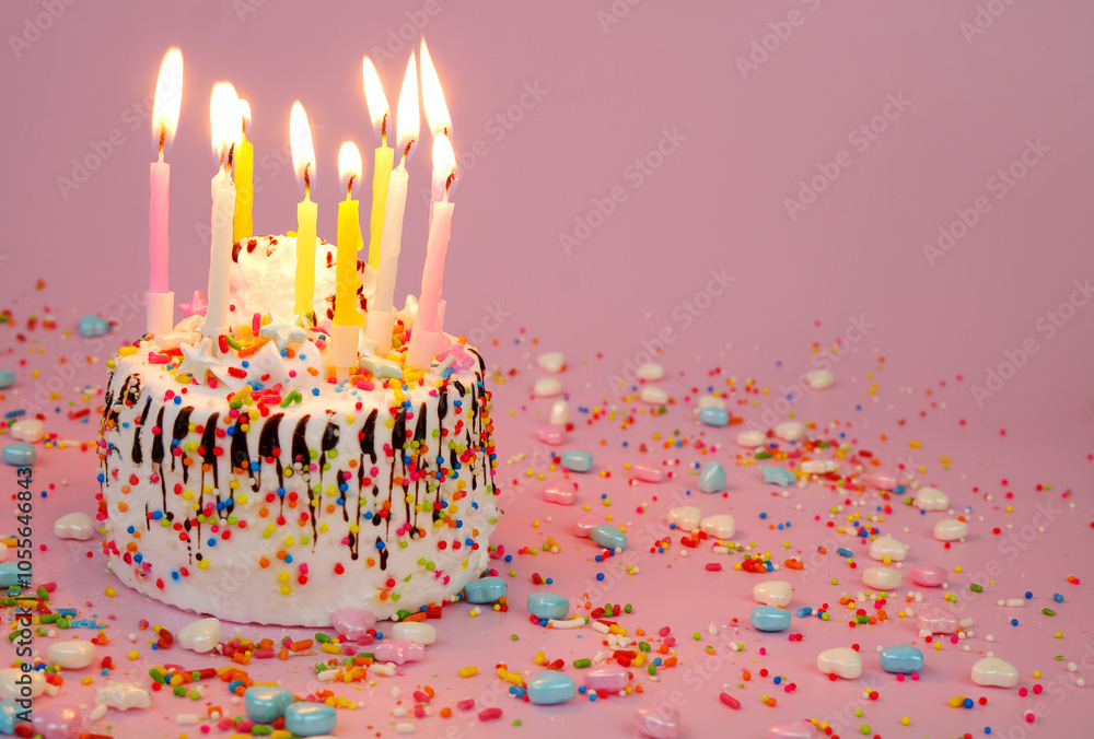 Birthday cake with burning candles and many sprinkles on pink background. Copy space for text. Birthday cake with burning candles and many sprinkles on pink background. Copy space for text.