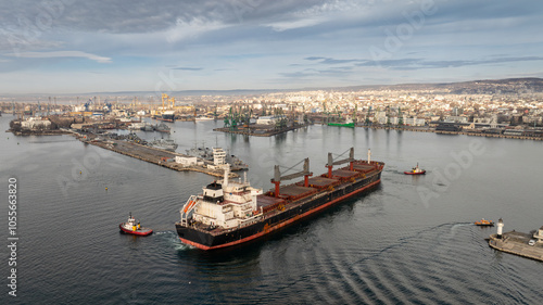 Aerial view of Tug boats assisting big cargo ship. Large cargo ship enters the port escorted by tugboats.