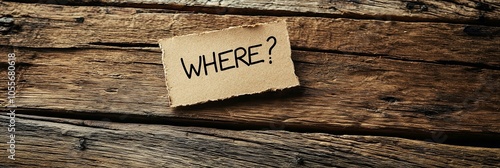 A rectangular piece of paper with the word 'WHERE?' lies on a textured plank of wood, symbolizing the quest for direction or location amidst life's path. photo