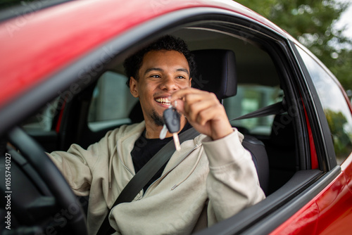 Young man holding car key inside red vehicle