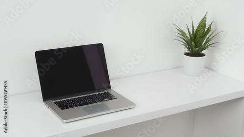 A closed laptop sits on a white desk with a green plant to the right.