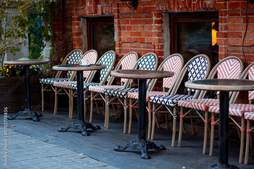 Obraz premium Multi-colored beautiful wicker chairs stand on a city street along the brick wall of a restaurant on a background of wooden round tables