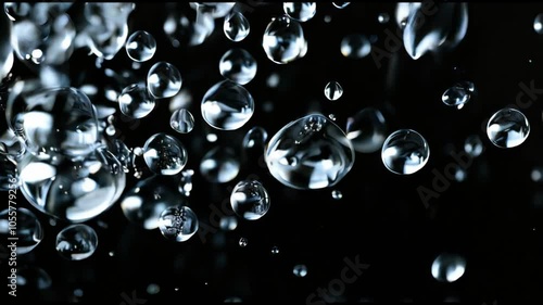 High-definition video of water droplets suspended in slow motion against a dark black background, highlighting their reflective and transparent qualities, perfect for themes of purity, nature, and cal