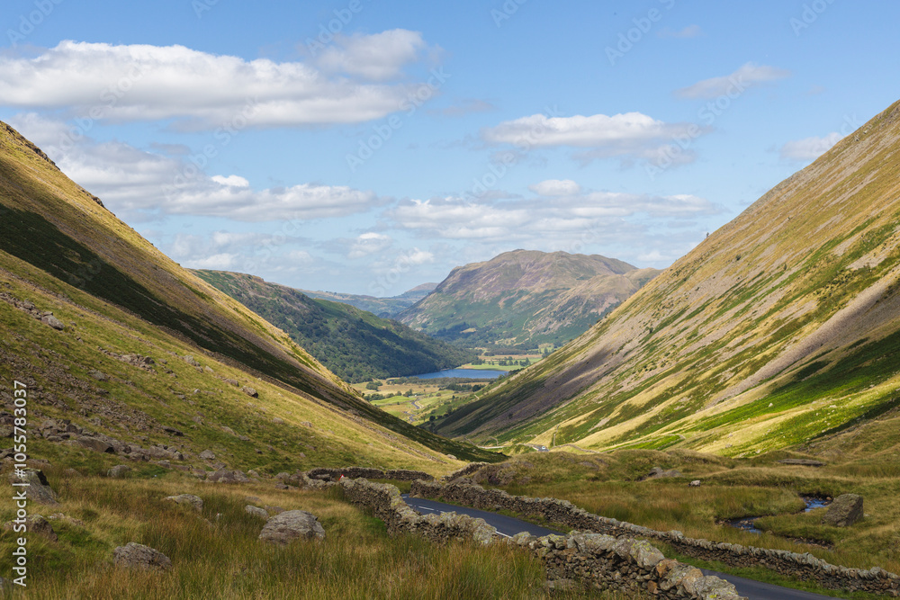 View of scenic winding road through beautiful green valleys and majestic mountains under a cloudy sky, Lake District, England. View of scenic winding road through beautiful green valleys and majestic mountains under a cloudy sky, Lake District, England.