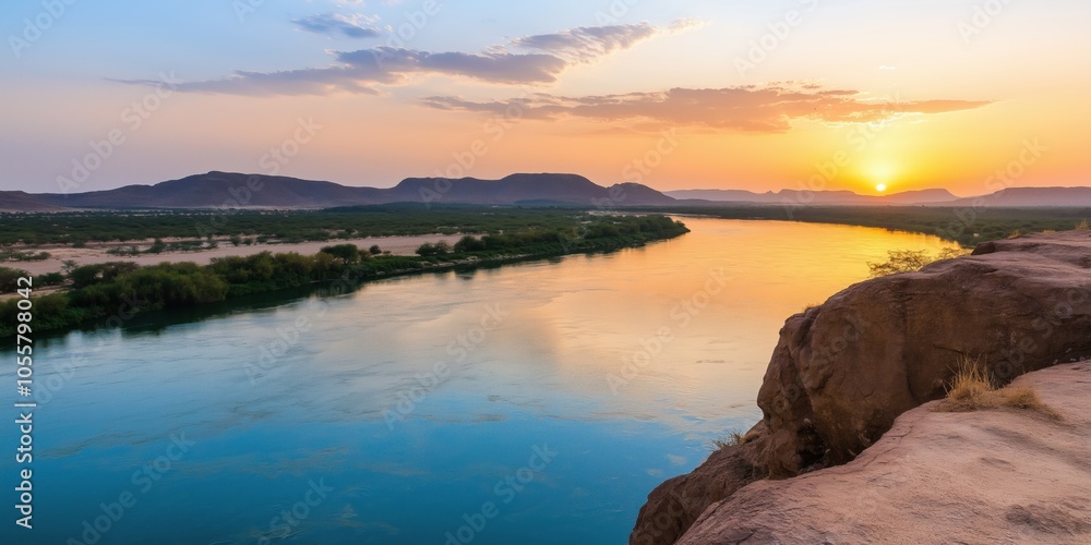 Fototapeta premium A beautiful sunset over a river with a rocky shoreline. The water is calm and the sky is filled with warm colors