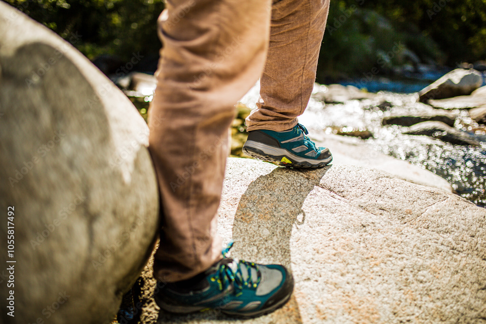 Person standing on rocks with hiking shoes near a river Person standing on rocks with hiking shoes near a river