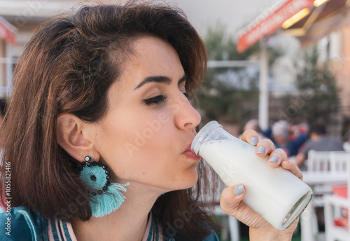 Woman drinking fresh ayran (buttermilk) from a glass bottle, enjoying a refreshing moment outdoors.