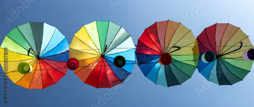 A vibrant display of colorful shadows hang suspended over a clear blue sky.The umbrellas are arranged in a row, creating a rainbow-like effect. The image evokes a sense of joy, creativity and optimism photo