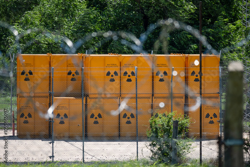 Foto Group of yellow barrels stacked with radioactive waste, behind a ball of barbed wire