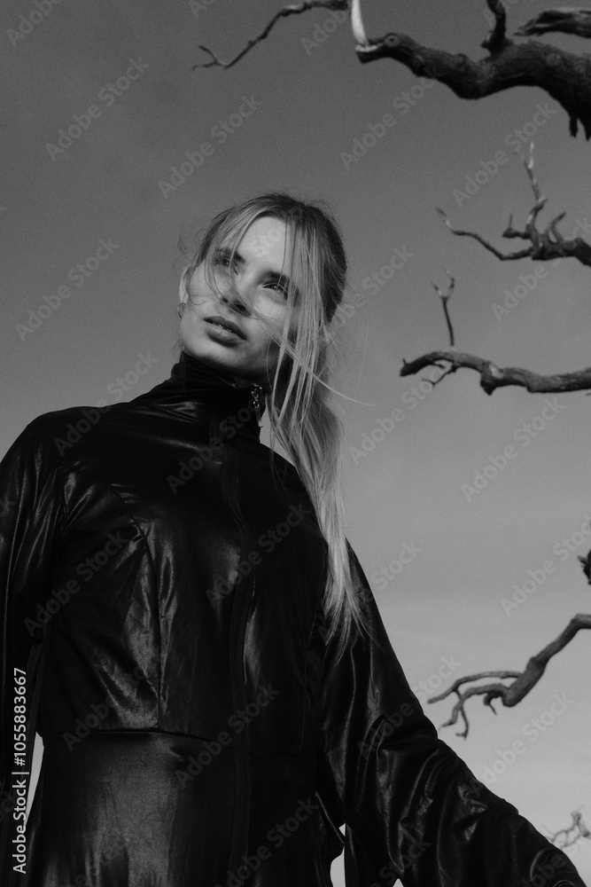 Fototapeta premium Fashion portarait of a young blonde girl in black strange dress. Autumn nature and tree branches. Black and white