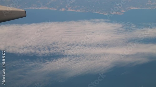 Flying on the airplane over the fluffy clouds under the wing through the plane window of an aircraft. Aerial view photo