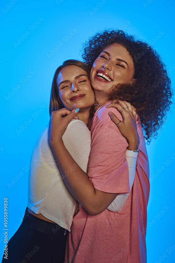 Two happy women share a loving embrace, celebrating their diversity against a playful pink backdrop. Two happy women share a loving embrace, celebrating their diversity against a playful pink backdrop.