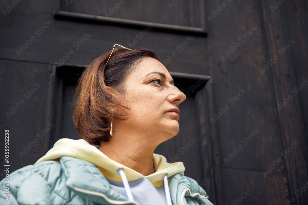 Thoughtful woman in hoodie and jacket against dark wooden door Thoughtful woman in hoodie and jacket against dark wooden door