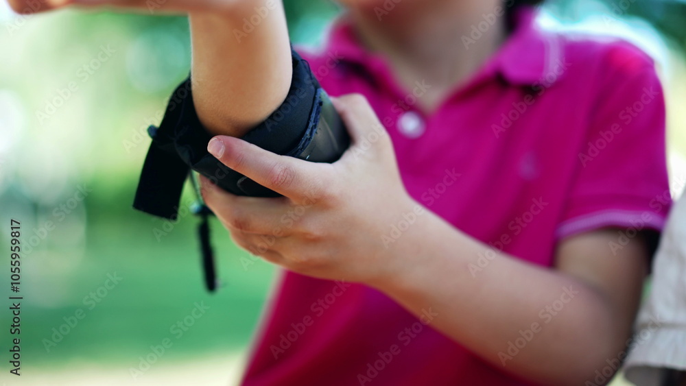 Close-up of a young boy adjusting his wrist guard, focusing on securing protective gear for outdoor activities, showing attention to safety and readiness before play Close-up of a young boy adjusting his wrist guard, focusing on securing protective gear for outdoor activities, showing attention to safety and readiness before play