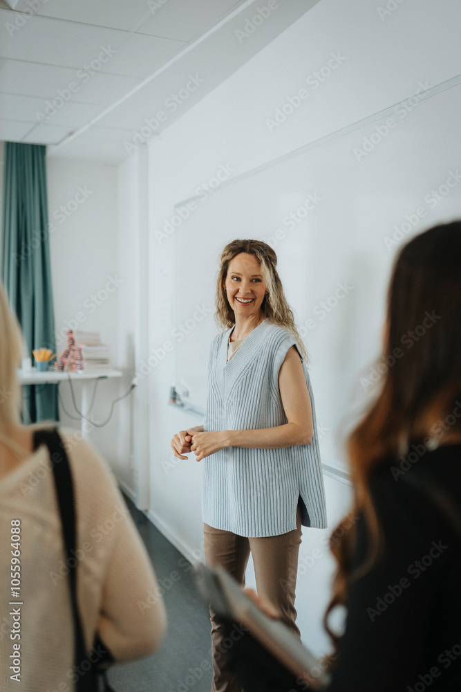 Smiling teacher looking at female students while standing against whiteboard in classroom Smiling teacher looking at female students while standing against whiteboard in classroom