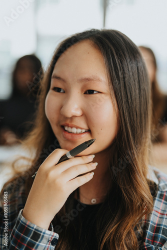 Smiling teenage girl holding pen with hand on chin at high school