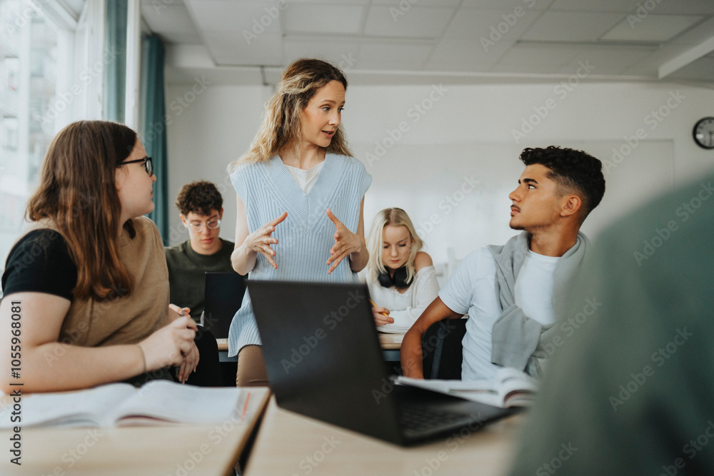 Female teacher gesturing while explaining to teenage boy and girl in classroom Female teacher gesturing while explaining to teenage boy and girl in classroom