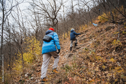 Two individuals are hiking up a hill in a beautiful wooded area, surrounded by tall trees and lush greenery, enjoying the fresh air and natural landscape on their outdoor adventure