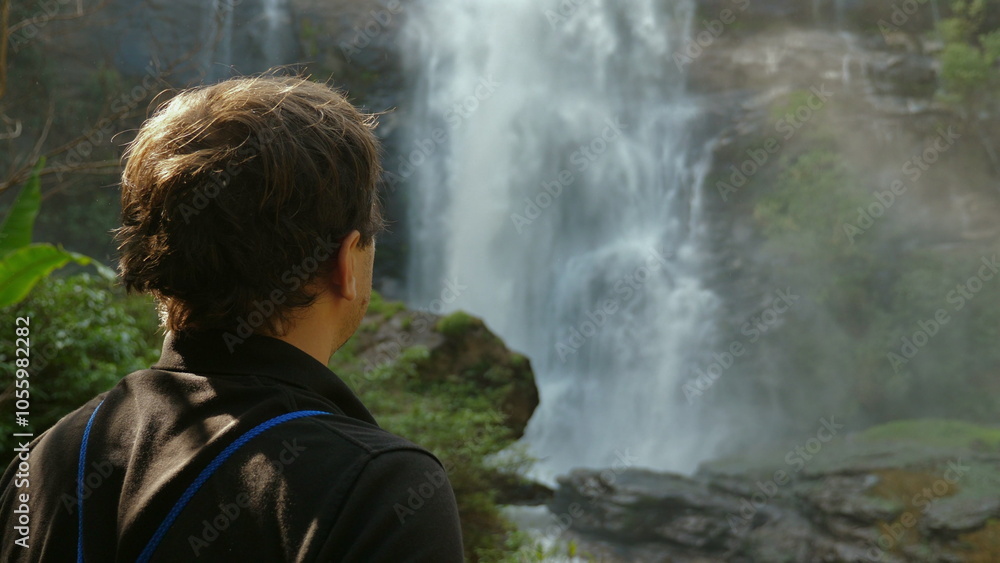 Fototapeta premium Person Admiring Majestic Waterfall in Lush Forest, Nature and Relaxation.