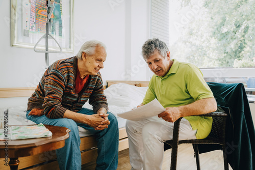 Male nurse reading medical reports to elderly man sitting on bed at retirement home photo