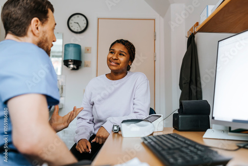 Male doctor explaining young women while sitting near table at medical examination room photo