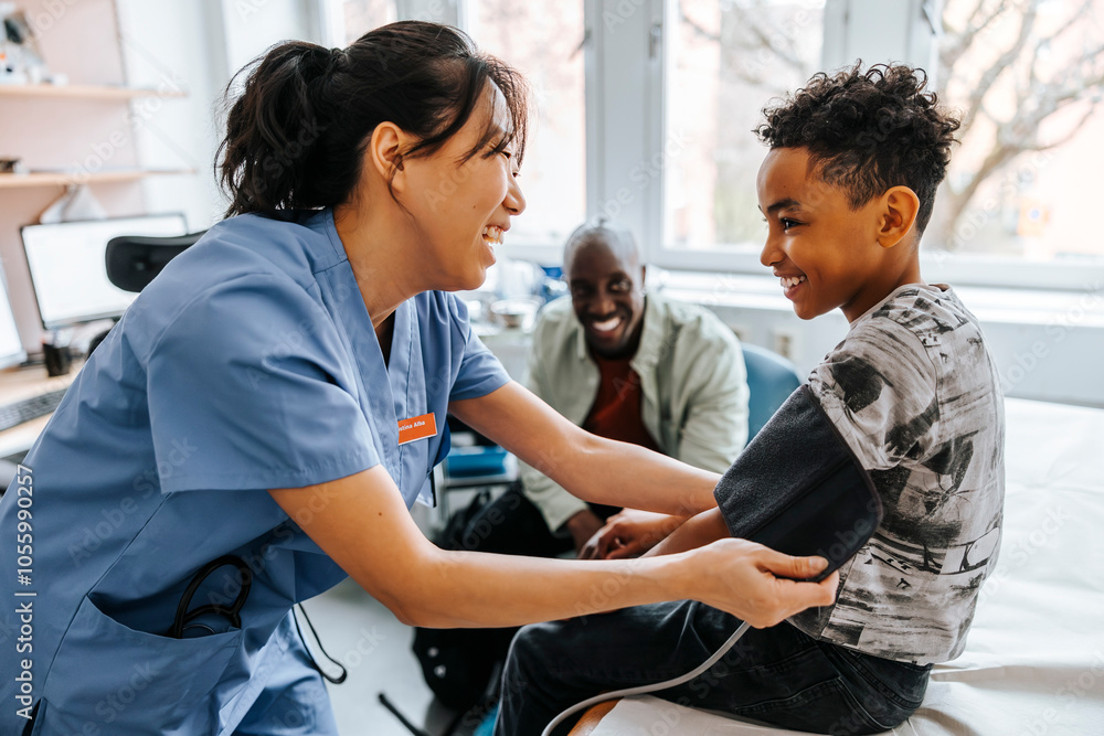 Happy female pediatrician checking boy's blood pressure in examination room Happy female pediatrician checking boy's blood pressure in examination room