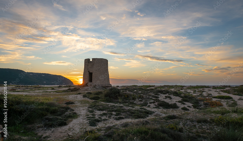 An old stone windmill on a beach at sunset with stunning sunlight and sky clouds. An old stone windmill on a beach at sunset with stunning sunlight and sky clouds.