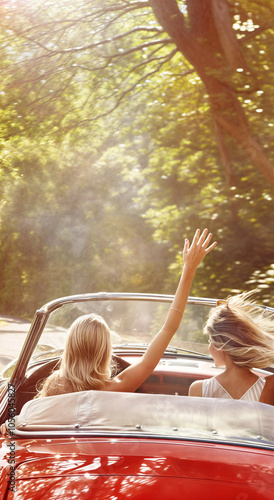 Two girls traveling by car, waving to people, rear view. Outdoor road trip photography