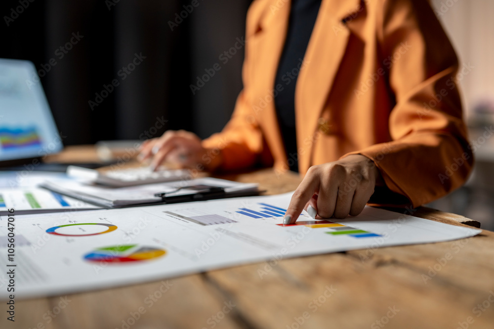 Businesswoman analyzing financial charts and using calculator at office desk Businesswoman analyzing financial charts and using calculator at office desk