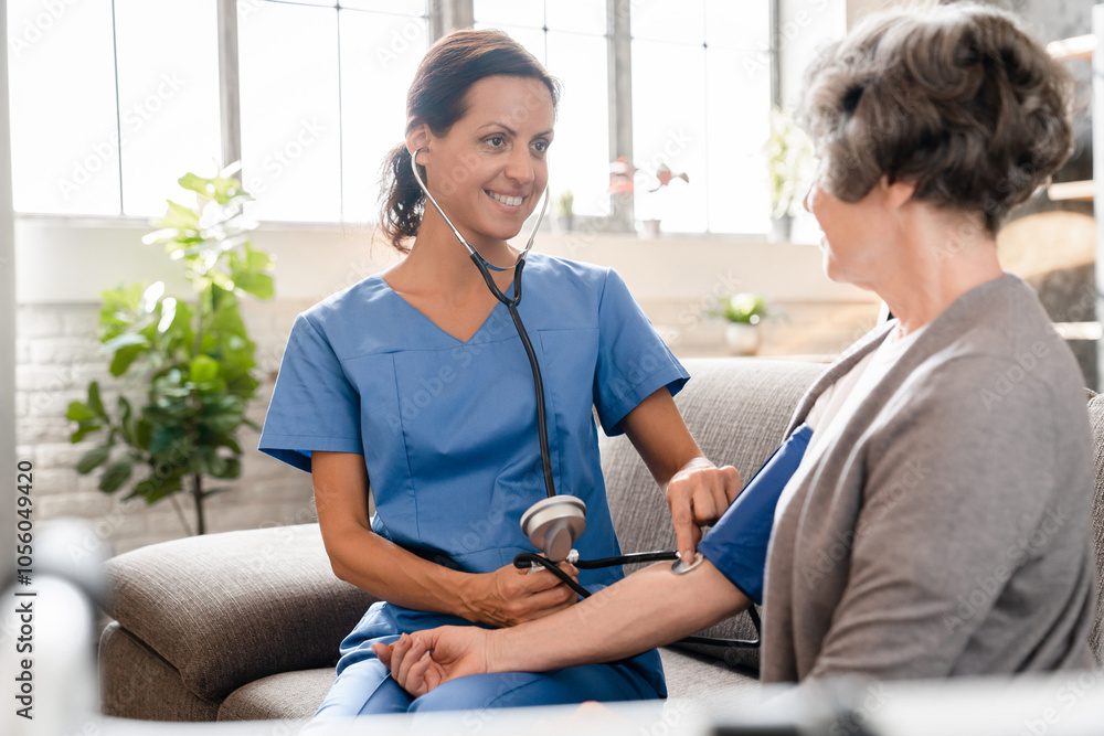 Fototapeta premium Mature smiling nurse caregiver doctor medical worker checking pulse and blood pressure of old elderly senior patient grandmother at home hospice. Hypertension illness