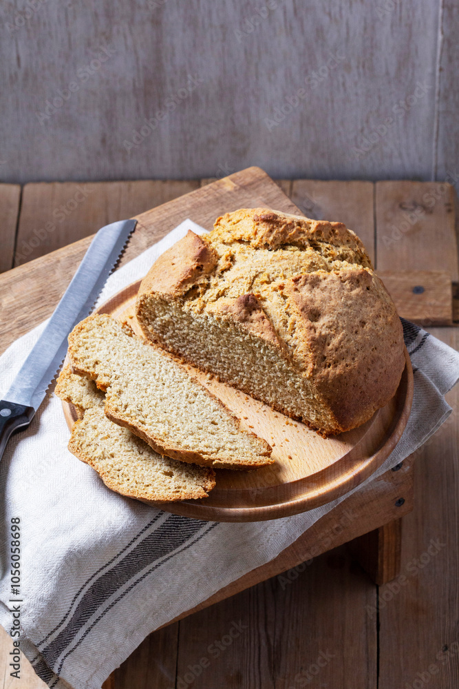 Homemade Irish soda bread cut into pieces and knife on wooden background.
