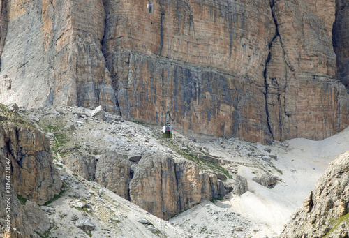 view of the cable car that looks tiny amidst the rocky walls of the mountain called Sass Pordoi in the Dolomites of the European Alps in Northern Italy photo